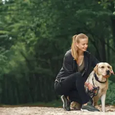 Kobieta w lesie kuca przy psie, głaszcze go po głowie.
